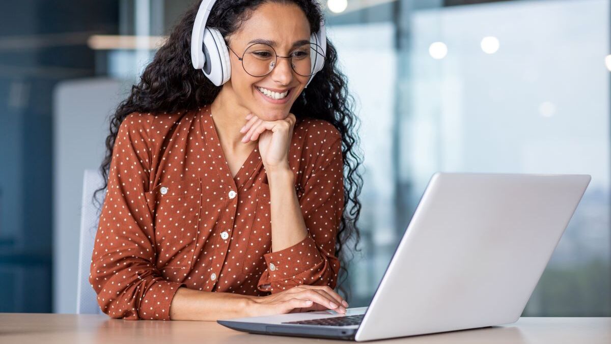 Das Bild zeigt eine junge Zahnärztin, die gut gelaunt an ihrem Laptop ein Webinar der Just Dent It Online Edition für eine erfolgreiche Praxisführung verfolgt.